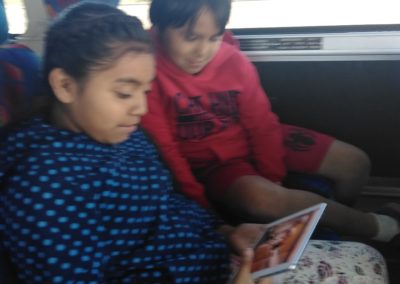 Two children sitting on a bus looking at an ipad.