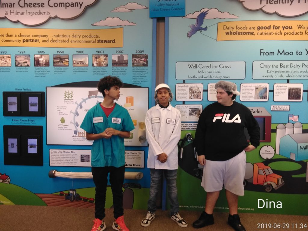 Three kids standing in front of a wall with pictures on it.