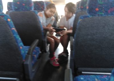 Two people sitting on a bus looking at their cell phones.