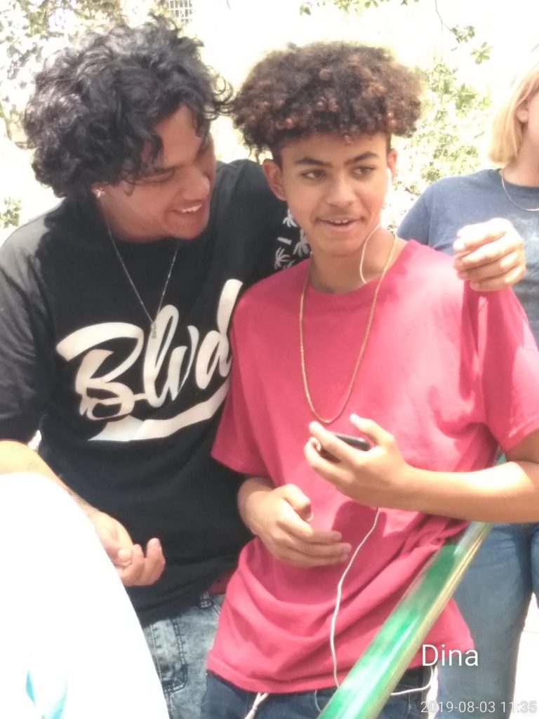 Two young men are standing together and one is holding a cell phone.